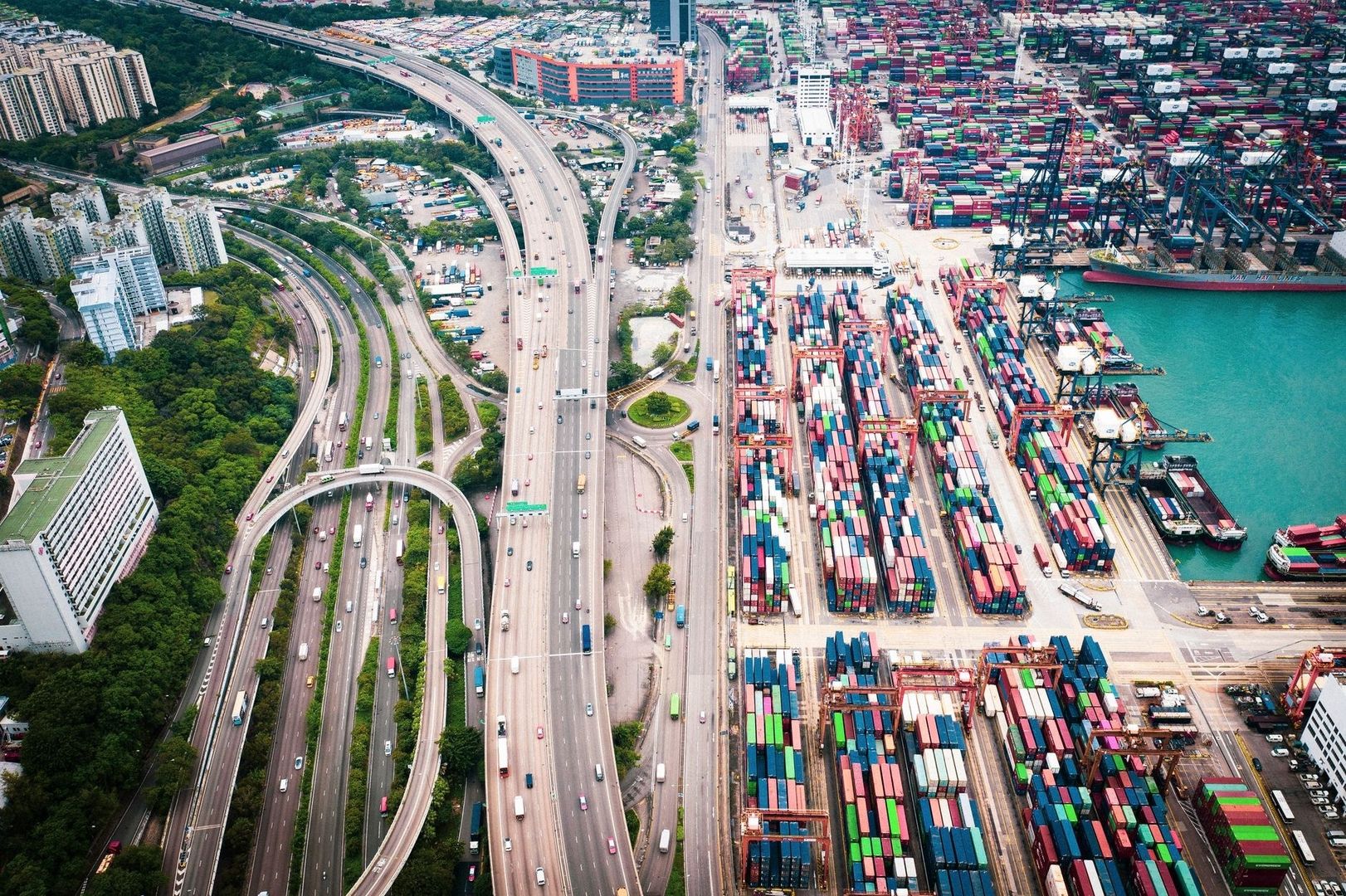 Luftfoto af motorveje, containerterminal og fragtskib ved en travl havn